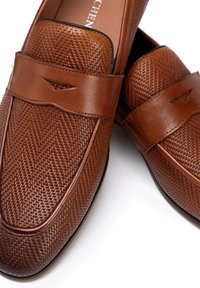 Braune Lederloafers mit strukturiertem Woven-Design, flacher Form, runder Zehenpartie und schmalem Riemen über der Vorderseite.