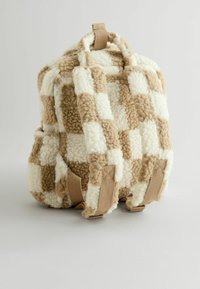 Sac à dos à carreaux marron et blanc en tissu duveteux, avec deux bretelles ajustables et une poignée supérieure pour le transport.