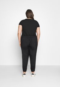 Svart t-shirt med kort ärm och svarta joggarbyxor med elastisk midja och ankelslut, i kombination med vita sneakers med svarta detaljer.