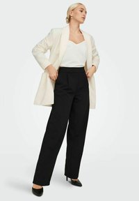Blazer blanc sur un débardeur blanc, associé à un pantalon noir à taille haute et des escarpins noirs à talons pointus. Textures lisses et coupe ajustée.