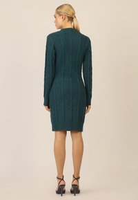 Teal strikket kjole med diamantmønstre, lange ærmer og ribbet kant. Matchet med sorte strophæle. Bagfra.