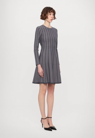 Vestito navy con maniche lunghe e gonna a ruota. Presenta un motivo geometrico e un corpetto aderente. Indossato con scarpe con tacco alto nere.
