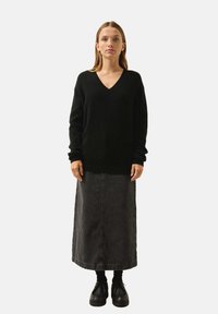 Schwarzer V-Ausschnitt-Pullover mit langen Ärmeln, kombiniert mit einem langen Jeansrock in dunkler Waschung und robusten schwarzen Schuhen. Einfaches Design mit lässigem Schnitt.