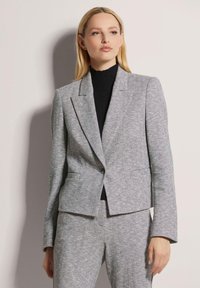 Grau-hahnentrittmuster Blazer in taillierter Passform mit Reverskragen, einreihiger Knopfschluss und zwei Fronttaschen, kombiniert mit einem schwarzen Rollkragenpullover.