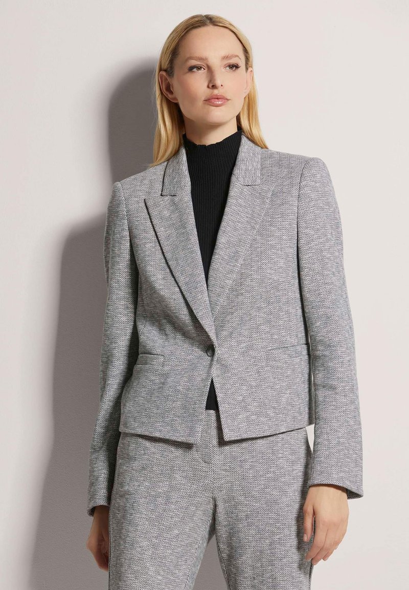 Grau-hahnentrittmuster Blazer in taillierter Passform mit Reverskragen, einreihiger Knopfschluss und zwei Fronttaschen, kombiniert mit einem schwarzen Rollkragenpullover.