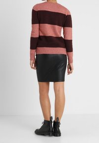 Sweter w paski w kolorze różowym i ciemnobrązowym, zestawiony z czarną ołówkową spódnicą ze skóry. Całość dopełniają czarne sznurowane botki.