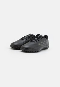 Zapatos de fútbol negros hechos de cuero sintético con una textura suave, que cuentan con un diseño de cordones y suelas de goma con pequeños tacos.