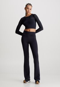 Top crop lungo nero a maniche lunghe con dettagli in rete e leggings flared abbinati a vita alta, realizzati in tessuto elasticizzato per il massimo comfort.