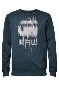 Mörkblå långärmad sweatshirt med en vit förvriden vertikal linjegrafik och delvis dold text på framsidan.