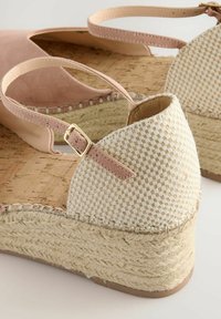 Roza suede visoke sandale s pletenim bež plitkim podnožjem, trakom oko gležnja s zlatnom kopčom i teksturiranim jute detaljima na potplatu.