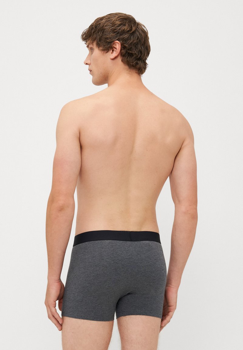 Grijze katoenen boxershorts met een zwarte tailleband, aansluitend ontwerp en een gladde textuur, weergegeven vanuit de achterkant op een naakte torso.