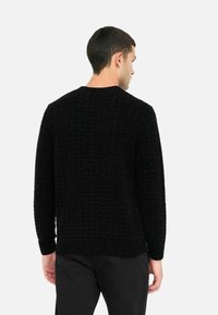 Maglione nero a maglia con un motivo testurizzato, scollo rotondo, maniche lunghe e polsini a costine. La vista posteriore mostra una vestibilità rilassata e dettagli sottili.