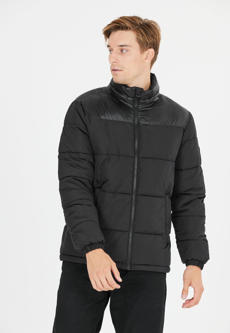 Sort polstret jakke med høj krave, lynlåslukning, elastiske manchetter og en quiltet design. Stoffet har en glat, mat tekstur.