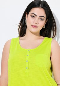 Top sin mangas de color verde lima con escote redondeado, tapeta con botones, bolsillo en el frente y textura suave.