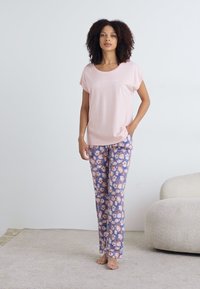 Šviesiai rožinė trumpomis rankovėmis marškinėliai su balta tekstu. Suderinti su mėlynomis pižamos kelnėmis, turinčiomis gėlių raštą rožių, baltos ir oranžinės spalvų atspalviais.