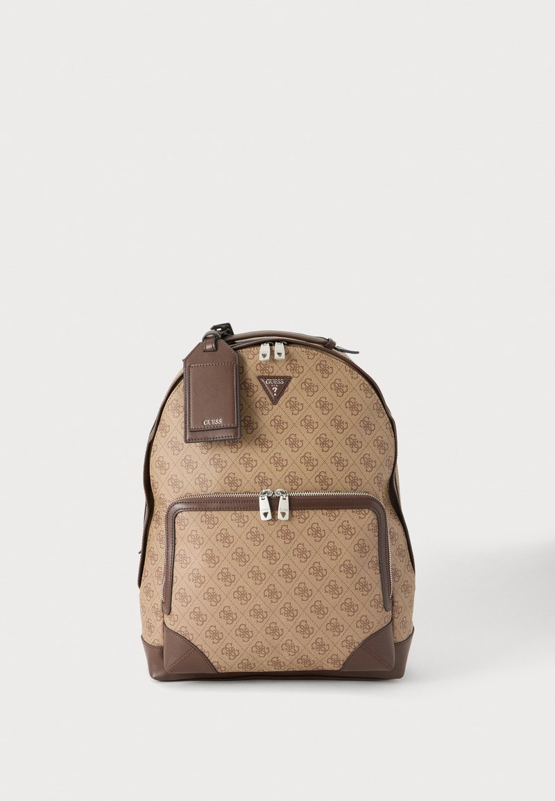 Sac à dos Guess marron à motifs avec poche avant zippée, garniture en cuir et étiquette rectangulaire en cuir attachée sur fond clair.