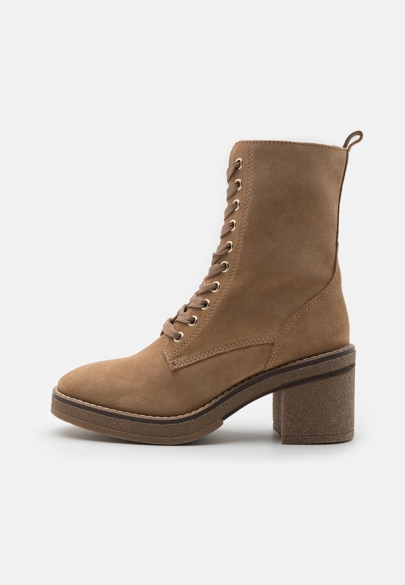 Bottine en daim marron avec bout rond, fermeture à lacets sur l’avant et œillets dorés. Dotée d’un talon épais texturé et d’une couture contrastante sur la semelle.