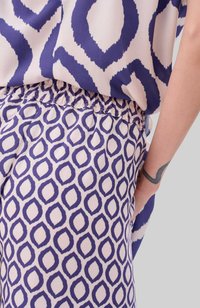 Blouse met abstract marineblauw patroon op lichte stof overlapt met gestreepte marineblauwe en crèmekleurige broek met een geraffineerde tailleband en zijzakken.