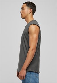 Chemise sans manches en coton gris avec une coupe décontractée, encolure ronde et bords bruts, associée à un jeans en denim bleu. Vue de côté affichée.