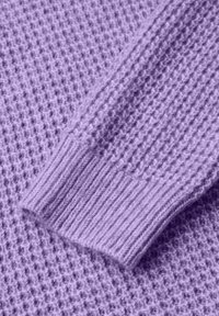 Pull en laine lavande avec un motif texturé. Les poignets à côtes présentent une finition lisse. Le tissu est doux et légèrement duveteux.