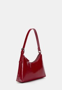 Red synthetic leather handbag with a curved silhouette, adjustable strap, and a zip closure. Smooth texture and sleek design.