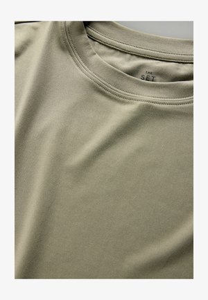 Õline rohelise tooniga T-särk, valmistatud pehmest ja siledast kangast; iseloomulik ümmargune kaelus ja õmblustega detailid ümber krae.