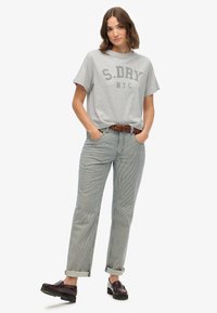 Grijs katoenen T-shirt met "S.DRY N.Y.C." in donkergrijs erop gedrukt, gecombineerd met ontspannen gesneden broeken in blauw en wit met strepen en een bruine riem.