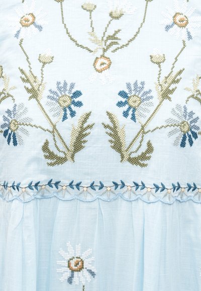 Ανοιχτό μπλε ύφασμα με σταυροβελονιά λουλουδένιο σχέδιο σε μπλε, άσπρο, πράσινο και μπεζ, με μαργαρίτες και φυλλώδεις βλαστούς.