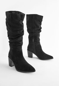Bottes hautes en daim noir au-dessus du genou avec un design décontracté, un bout pointu et un talon bloc. Elles disposent d'une fermeture éclair latérale pour un enfilage facile.