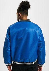 Blauwe bomberjas met een glanzende afwerking, voorzien van een zwart-wit gestreepte geribde kraag en manchetten, en een elastische zoom.