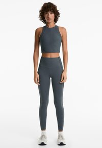 Ensemble de vêtements de sport gris foncé comprenant un crop top sans manches avec un col montant et un legging taille haute au toucher lisse.