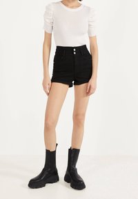 Svarta högmidjade denimshorts med rullade sidsömmar, tillsammans med en vit ribbad topp och kraftiga svarta läderstövlar i ankellängd.