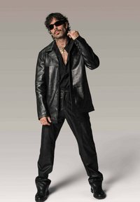 Veste en cuir noir avec un devant à boutons, associée à un pantalon en cuir noir assorti et des bottes. L'arrière-plan est un dégradé neutre.