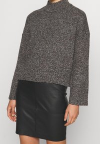 Grauer gestrickter Pullover mit hohem Kragen, fallenden Schultern und kurzer Passform, kombiniert mit einem schwarzen Minirock aus Leder, glatte Textur.