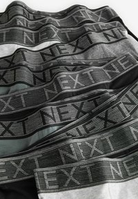Vīriešu apakšveļa, kas pieejama dažādās krāsās: melna, pelēka un gaiši pelēka. Katram ir melna un sudraba svītrains elastīgs jostasvads ar uzrakstu "NEXT".