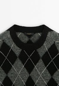Pull en tricot avec un motif argyle noir et gris, un col rond et une texture douce. Étiquette visible au col.
