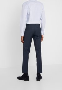 Navy farbige maßgeschneiderte Hose mit schlanker Passform, aus gewebtem Stoff, mit zwei Gesäßtaschen, kombiniert mit einem hellblauen Langarmhemd.
