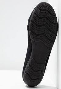 Semelle de chaussure noire avec motif de bande de roulement ondulée affichée verticalement sur fond blanc.