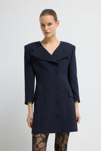 Cappotto navy a doppio petto con ampi rever e sei bottoni. Realizzato in tessuto liscio, presenta tasche laterali e una forma strutturata.