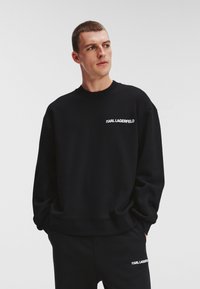 Sudadera negra de tejido suave con cuello redondo, que presenta el logo blanco "KARL LAGERFELD" en el pecho y una silueta de corte relajado.