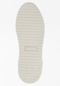 Suola di scarpa in gomma con texture esagonale, colore beige chiaro. Logo "GUESS" impresso al centro. Punta e bordi del tallone arrotondati.