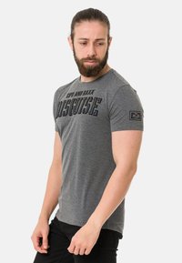 Graues Baumwoll-T-Shirt mit kurzen Ärmeln, das auf der Vorderseite schwarzen grafischen Text "CIPO AND BAXX" und "DISGUISE" zeigt, mit einem Logo-Patch am Ärmel.