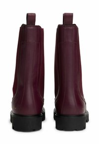 Un par de botas de tobillo de cuero burdeos oscuro con tiradores y suelas de goma negra gruesa, vistas desde la parte de atrás.