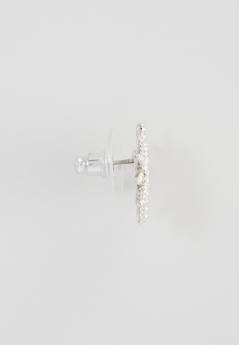 Boucle d'oreille en argent avec un motif floral décoratif, arrière transparent et surface polie, dotée d'un clou rond pour le maintien.