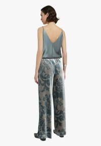 Top in seta color azzurro chiaro con scollo a V sul retro, abbinato a pantaloni a gamba larga con motivo floreale grigio e blu e vita con coulisse.