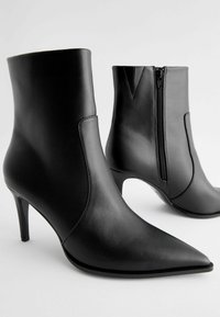 Bottines en cuir noir avec un bout pointu, un design effilé et une fermeture éclair sur le côté. Talon aiguille surélevé. Texture lisse avec un minimum de détails.
