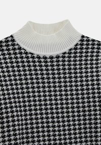 Juodo ir balto škotų langelių rašto megztinis su banguotu baltu golfo apykakle. Audinys atrodo minkštas ir megztas.