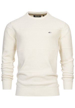 Suéter de punto color crema con un patrón texturizado, cuello redondo y puños y dobladillo acanalados. Presenta un pequeño logo azul en el pecho.