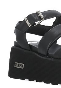 Sandali platform neri in pelle liscia, con una fascia dotata di una fibbia metallica e una suola testurizzata e scanalata. Logo del brand esposto.