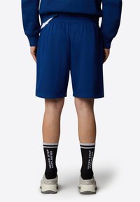 Pantalones cortos deportivos azules con cintura elástica, combinados con calcetines negros con texto blanco y zapatillas de deporte gris claro.